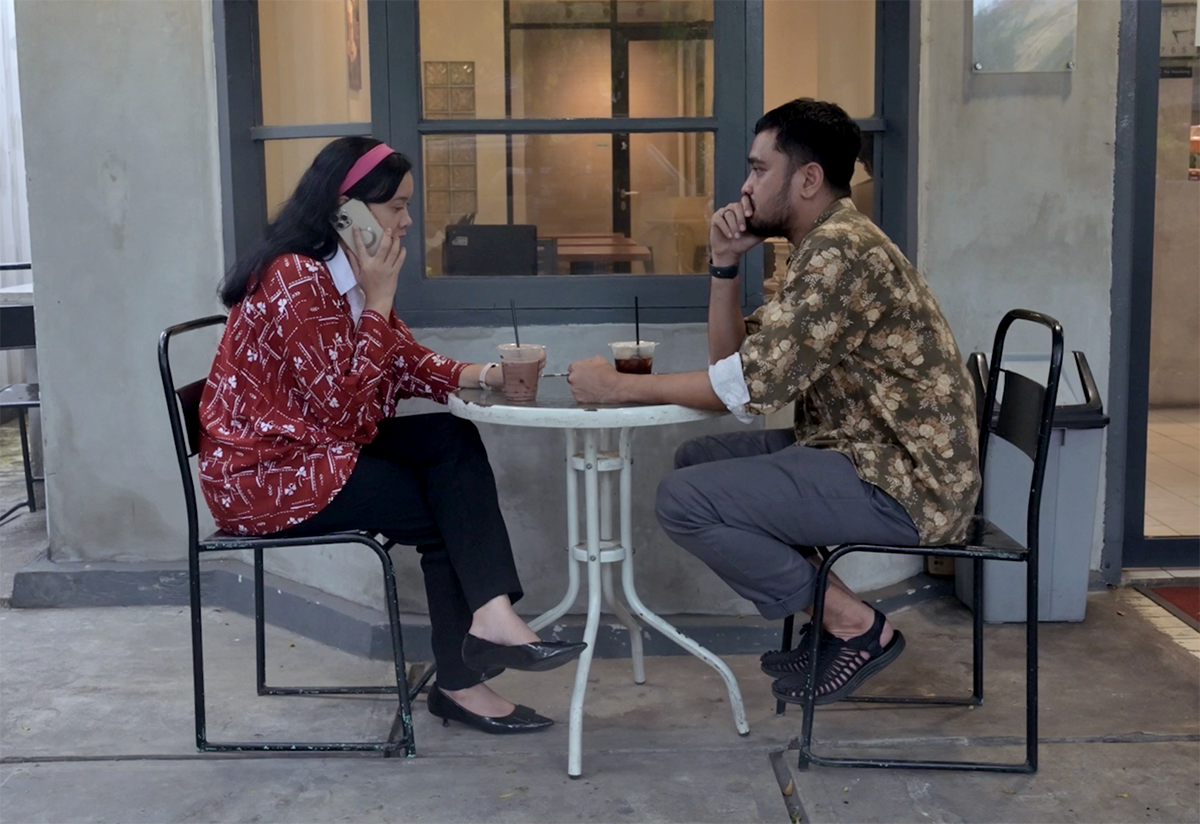 Ridhwan Siregar and Kiki Siregar sit at a café table, making calls during interview preparations.